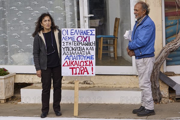 Two people at a protest, holding a sign with demands in Greek, Visit of Federal President Frank-Walter Steinmeier in Kandanos on 31 October 2024, Federal President, Frank-Walter Steinmeier, memorial, war crimes, Nazis, Wehrmacht crimes, World War II, Kandanos, southwest Crete, Crete, Greek islands, Greece, Europe