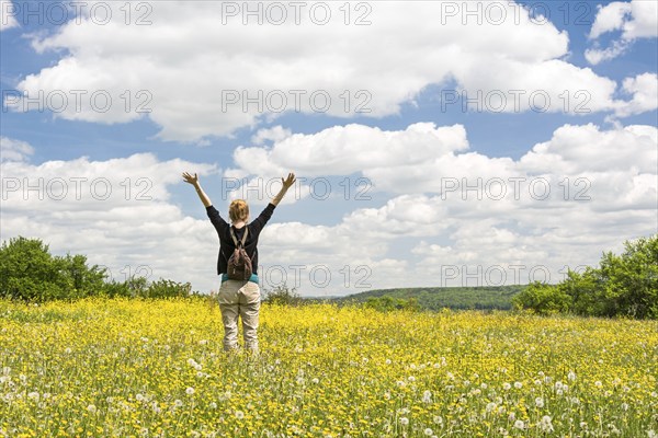 Rejoicing young woman standing on a flower meadow in summer