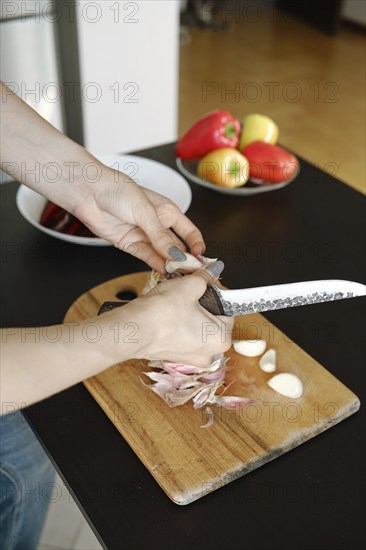Close-up view of female hands using kitchen knife to peel garlic cloves