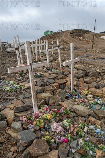 Row of graves with crosses and flowers on a stony cemetery under a grey sky, remote Arctic Inuit settlement Ittoqqortoormiit, Scoresbysund or Scoresby Sund or Greenlandic Kangertittivaq, East Greenland, Greenland, North America