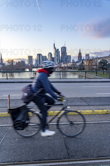 Skyline of the city centre of Frankfurt am Main, cyclist on the Ignatz-Bubis-Bridge, dusk, river Main, winter, Hesse, Germany, Europe