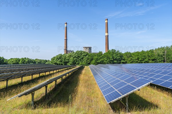 Solar modules of a solar park in front of the decommissioned Plessa lignite-fired power plant with two chimneys and cooling towers, Plessa, Lusatia, Brandenburg, Germany, Europe