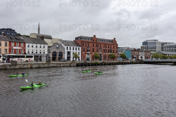 People paddling in kayaks on a river with industrial buildings in the background, Cork