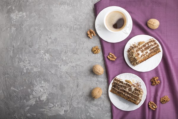 Homemade cake with milk cream and walnuts with cup of coffee on a gray concrete background and purple textile. top view, flat lay, copy space