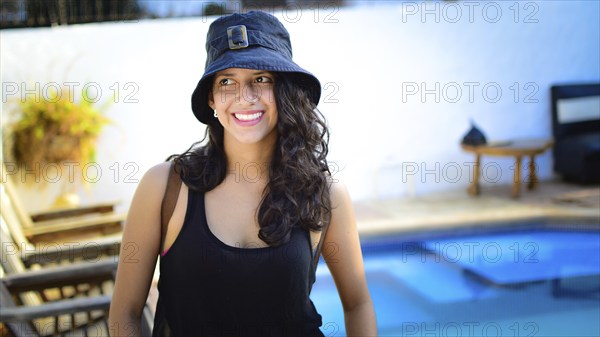 Portrait of pretty girl with hat smiling near a swimming pool. latin girl smiling with swimming pool in background