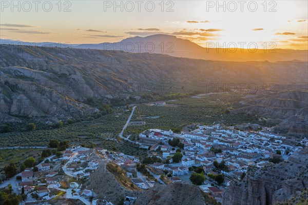 A village lies in a valley surrounded by hills and mountains as the sun sets and the valley glows in warm light, Gorafe, Guadix, Granada, Andalusia, Spain, Europe