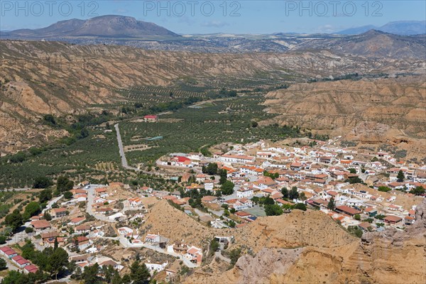 A small village with orange-coloured roofs is nestled in a green valley surrounded by mountains under a blue sky, Gorafe, Guadix, Granada, Andalusia, Spain, Europe