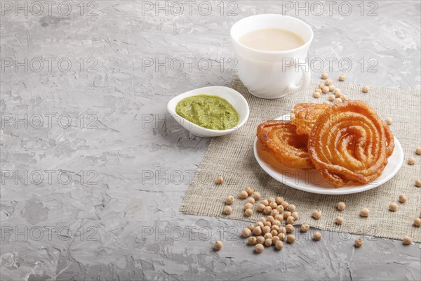 Traditional indian candy jalebi in white plate with mint chutney on a gray concrete background. side view, copy space