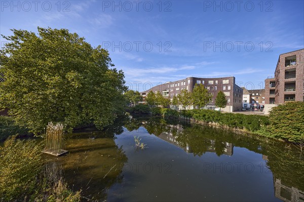 Trees and modern buildings are reflected on the surface of the Bocholter Aa river under a blue sky in Bocholt, Münsterland, Borken district, North Rhine-Westphalia, Germany, Europe
