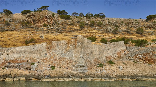 Old stone wall on rocky cliff with dry vegetation and calm sea water in the foreground, Venetian Sea Fortress, Leprosy Island, Spinalonga, Elounda Bay, Mirabello Bay, East Crete, Crete, Greek Islands, Greece, Europe