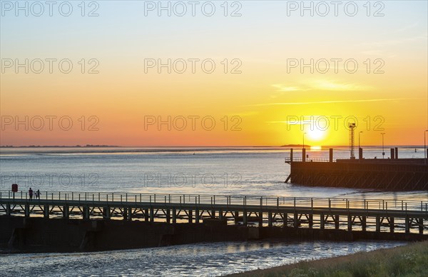 Silhouettes of several people on the pier Freilaufkanal, people watching from a jetty the picturesque, golden, breathtakingly beautiful sunset over the sea, far away islands Langlütjen I and II, harbour facilities, sun just above the horizon, orange glowing cloudless sky, wide sea in soft colours, calm atmosphere, mouth of the Weser into the North Sea, Outer Weser, Bremerhaven, Land Bremen, Germany, Europe