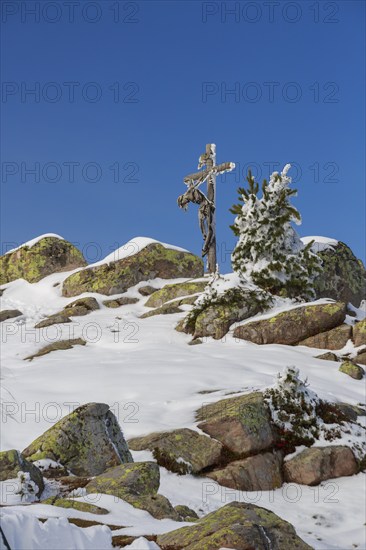 Wooden cross on snow-covered rocks, in front of it a clear blue sky in a wintry landscape