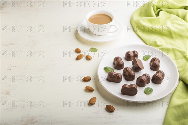 Chocolate candies with almonds and a cup of coffee on a white wooden background and green textile. side view, copy space