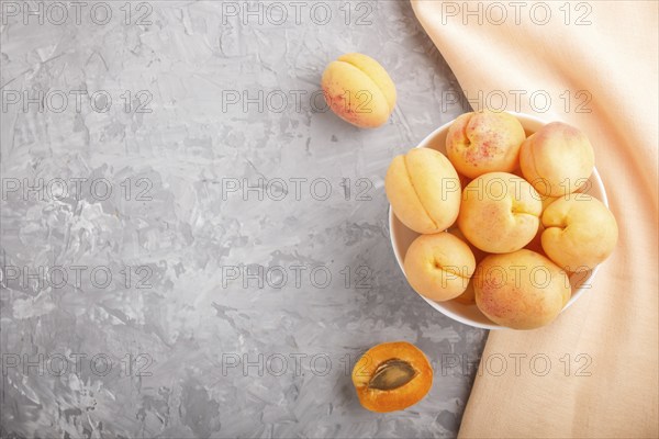 Fresh orange apricots in white bowl on gray concrete background. top view, copy space, flat lay