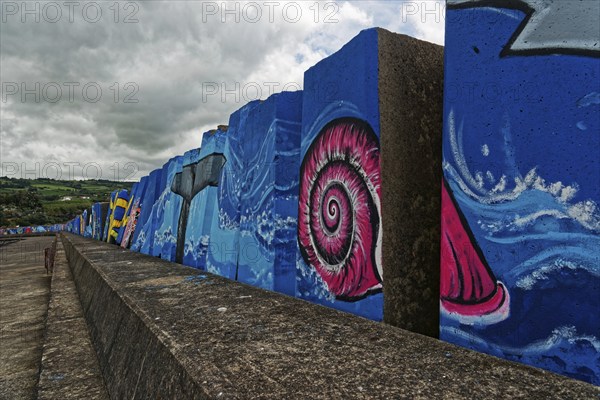 Colourful mural by the sea with a large pink snail under a cloudy sky, small town of Vila Franca do Campo, Sao Miguel, Azores, Portugal, Europe