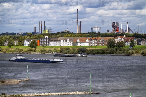 Cargo ship on the Rhine near Duisburg-Laar, houses on Deichstraße, industrial backdrop of the ThyssenKrupp Steel steelworks in Bruckhausen, North Rhine-Westphalia, Germany, Europe