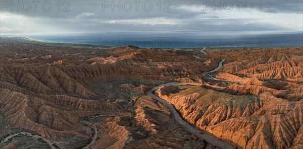 Riverbed runs through a landscape of eroded hills, badlands at sunset, Issyk Kul Lake in the background, aerial view, Canyon of the Forgotten Rivers, Issyk Kul, Kyrgyzstan, Asia