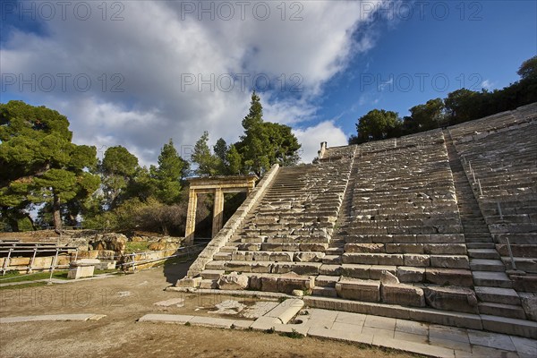 Partially restored amphitheatre under a blue sky next to green vegetation, Ancient Amphitheatre, Epidaurus, Peloponnese, Greece, Europe