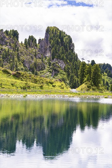 A clear mountain lake reflects the surrounding trees and mountains under a cloudy sky, Penken, Zillertal, Austria, Europe