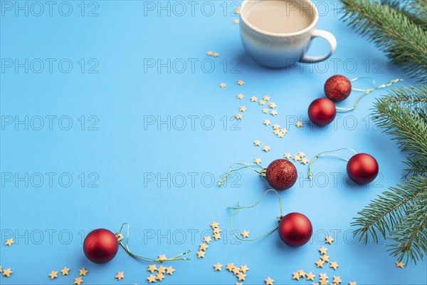 Christmas or New Year composition. Decorations, red balls, fir and spruce branches, cup of coffee, on a blue paper background. Side view, copy space