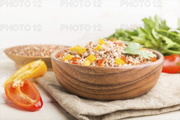 Buckwheat porridge with vegetables in wooden bowl on a white wooden background and linen textile. Side view, copy space, selective focus. Russian traditional cuisine