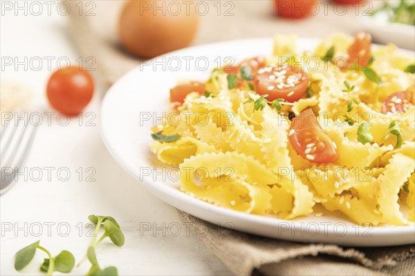 Reginelle semolina pasta with tomato, eggs, sesame and microgreen sprouts on a white wooden background and linen textile. Side view, close up, selective focus