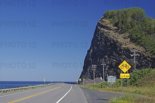 A road along a large cliff with a view of the sea and road signs indicating a cycle path, Gaspesie, St. Lawrence Srom, Quebec, Canada, North America
