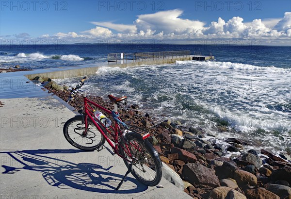 A red bicycle stands on the shore with a view of the rough sea and thick clouds in the blue sky, Tönsberg, Oslofjord, Norway, Europe