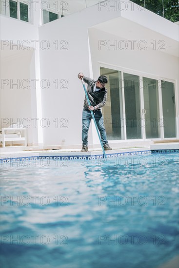 Maintenance person cleaning a beautiful home swimming pool. Worker cleaning a beautiful homemade swimming pool with skimmer