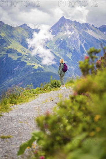 Woman enjoying the view of a picturesque mountain landscape on a hiking trail surrounded by colourful flowers, Penken, Zillertal. Austria