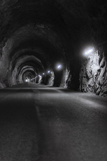Dark illuminated tunnel with rough rock faces and an asphalted road, Zillertal, Austria, Germany, Europe