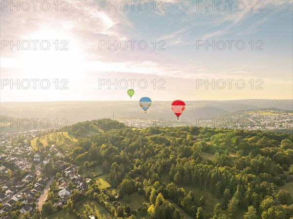 View of several hot air balloons over a wooded landscape at sunset near a town, Calw, Black Forest, Germany, Europe