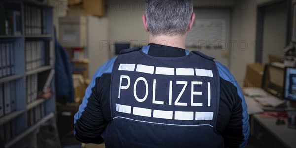 Police officer in office, back view, surrounded by files and computers, symbolic image search, Germany, Europe