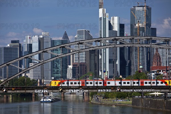 Main with regional railway on the Deutschherrnbrücke and a cargo ship in front of the skyline of Frankfurt am Main, Hesse, Germany, Europe