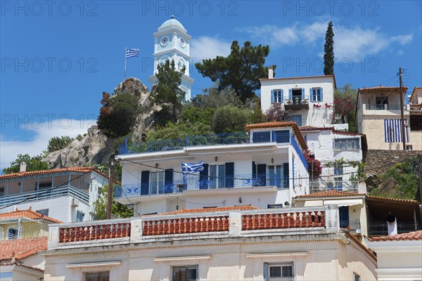 Picturesque Greek houses on a hill with a church and a Greek flag in front of it, blue and white clock tower, Poros, Poros Island, Saronic Islands, Peloponnese, Greece, Europe