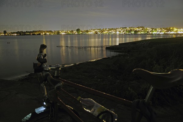 Night view of a lake with illuminated city in the background, bicycle in the foreground, Tönsberg, Oslofjord, Norway, Europe