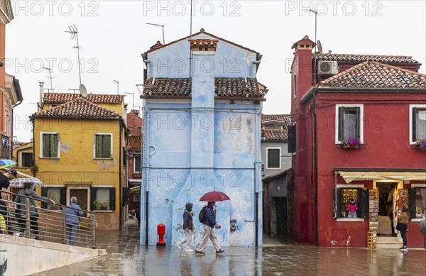 City view of Burano with colourfully painted houses and canals. Rainy weather, people are carrying umbrellas. Burano, Venice, Venezia, Italy, Europe