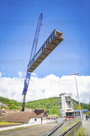 A crane lifts a bridge over a building complex in sunny weather with blue sky and white clouds, bridge lifting Hermann Hesse railway, Calw, Germany, Europe