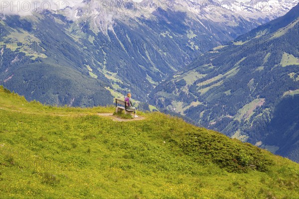 A woman sits on a bench and looks at the vast valleys and mountains, Penken, Zillertal, Austria, Europe