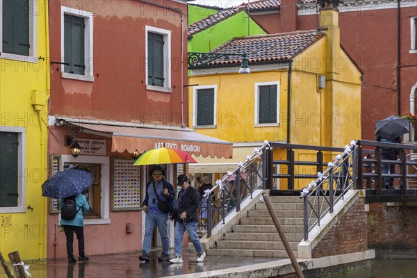 City view of Burano with colourfully painted houses and canals. Rainy weather, people are carrying umbrellas. Burano, Venice, Venezia, Italy, Europe