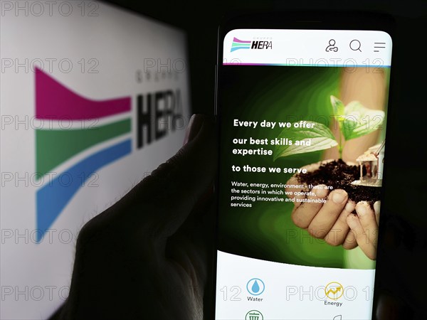 Stuttgart, Germany, 06-01-2024: Person holding cellphone with webpage of Italian utility company Hera S.p.A. in front of business logo. Focus on center of phone display, Europe
