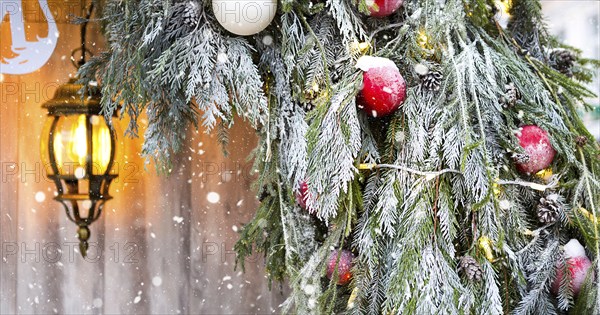 Outdoor Christmas decorations made of natural spruce branches, toys, garlands and a glowing lantern in the snow in a blizzard. Winter outside, snowfall. New Year decor