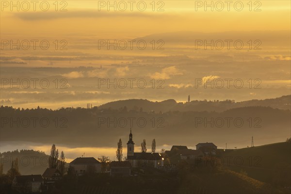 Autumn atmosphere in the golden morning light, fog drifts over the hilly landscape, silhouette of the church of Kitzeck, view from the Demmerkogel viewing platform, St. Andrä-Höch, Sausal wine country, Styria, Austria, Europe