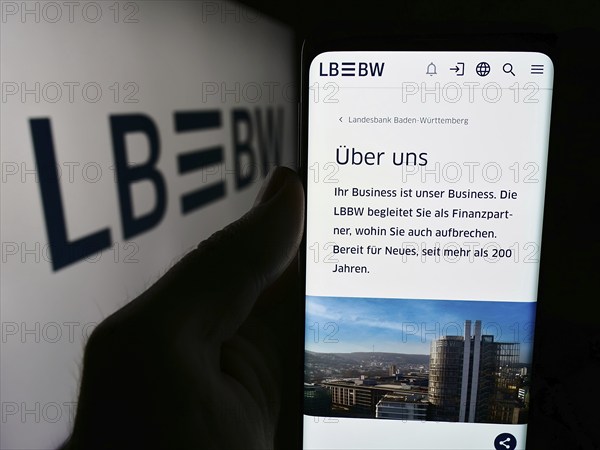 Stuttgart, Germany, 07-15-2024: Person holding cellphone with webpage of German company Landesbank Baden-Württemberg (LBBW) in front of logo. Focus on center of phone display, Europe