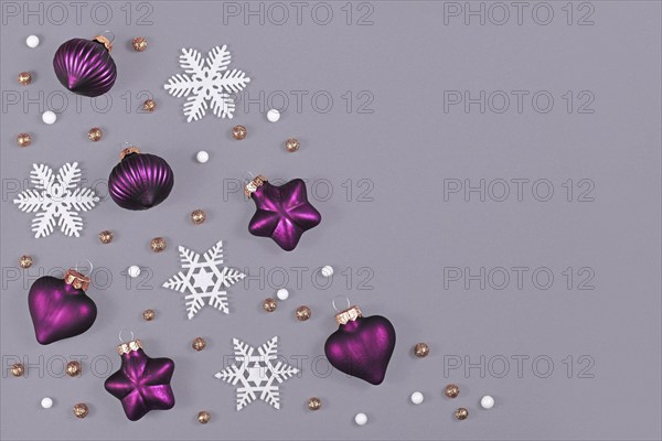 Christmas flat lay with purple heart and star shaped and round tree ornament baubles and white snowflakes on gray background with empty copy space on side