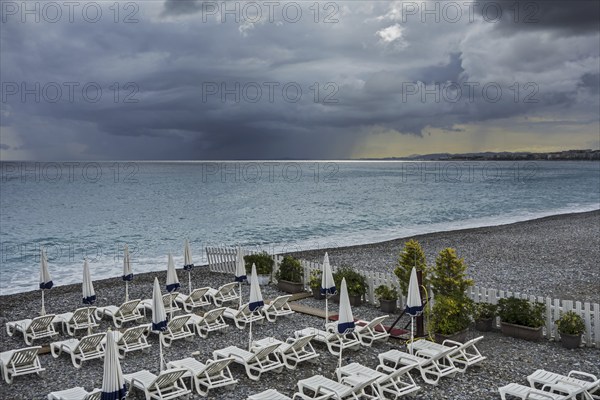 White reclining chairs on deserted beach during bad weather with dark, menacing rain clouds over the sea