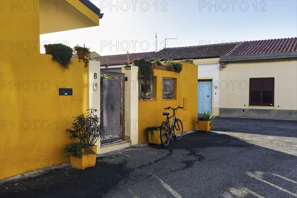 Potted plants and bicycle in front of a yellow house facade, Cabras, Oristano, Western Sardinia, Sardinia, Italy, Europe