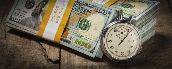 Time is money loan concept background, letterbox panorama of stopwatch and stack of new 100 US dollars 2013 edition banknotes (bills) bundles on wooden background