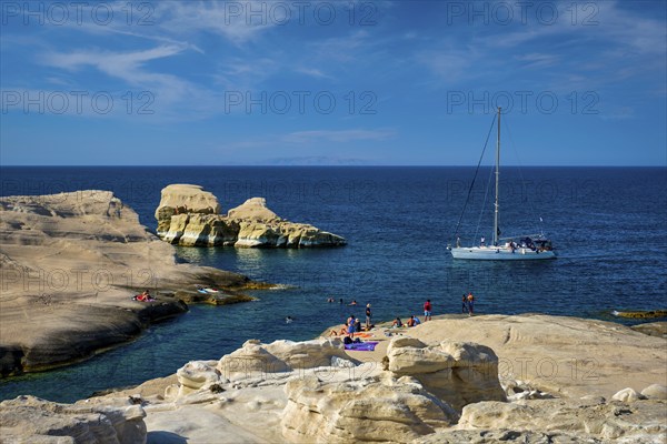 Yacht boat at famouse Sarakiniko beach white rocks tourist attraction with tourists on beach in Aegean sea on sunset, Milos island, Greece, Europe