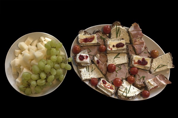 Plate with sandwiches and a plate with melon pieces and grapes on a black background, Mecklenbuirg-Vorpommern, Germany, Europe